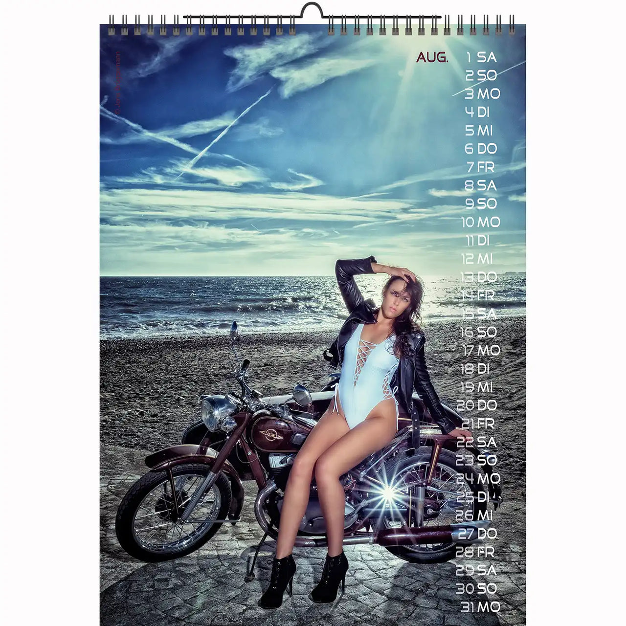 Brunette model in white bodysuit and jacket posing by a classic motorcycle on a seaside road – Bikes & Girls 2026 calendar