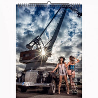 Calendar with a vintage car and two women in front of a large crane under a cloudy sky.