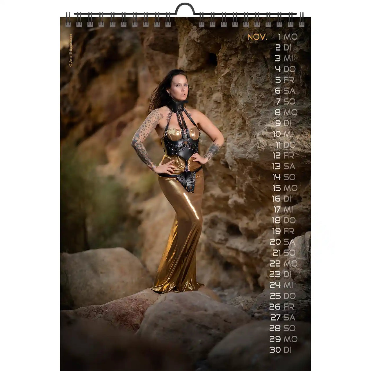 Kalender met een vrouw in een gouden en zwarte outfit die tegen een rotsachtige achtergrond staat