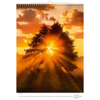 Kalenderpagina met een zonsondergang boven een boom, met warme kleuren en een zichtbaar merklogo.