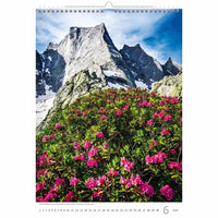 Kalenderpagina met een berglandschap met roze bloemen en een helderblauwe lucht.