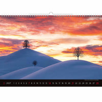 Kalender met een winterlandschap met besneeuwde heuvels en bomen tegen een kleurrijke avondrood.