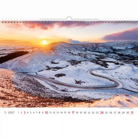 Kalender met een schilderachtig winterlandschap met een besneeuwde weg en zonsondergang.