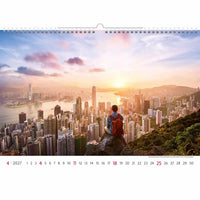 Kalender met een schilderachtig uitzicht op een stadsgezicht en een persoon met een rode rugzak, met een zonsondergang boven een groot stedelijk gebied.