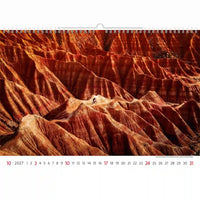 Kalender met een woestijnlandschap en een fietser op een berg, voorzien van een rood-oranje kleurenschema.