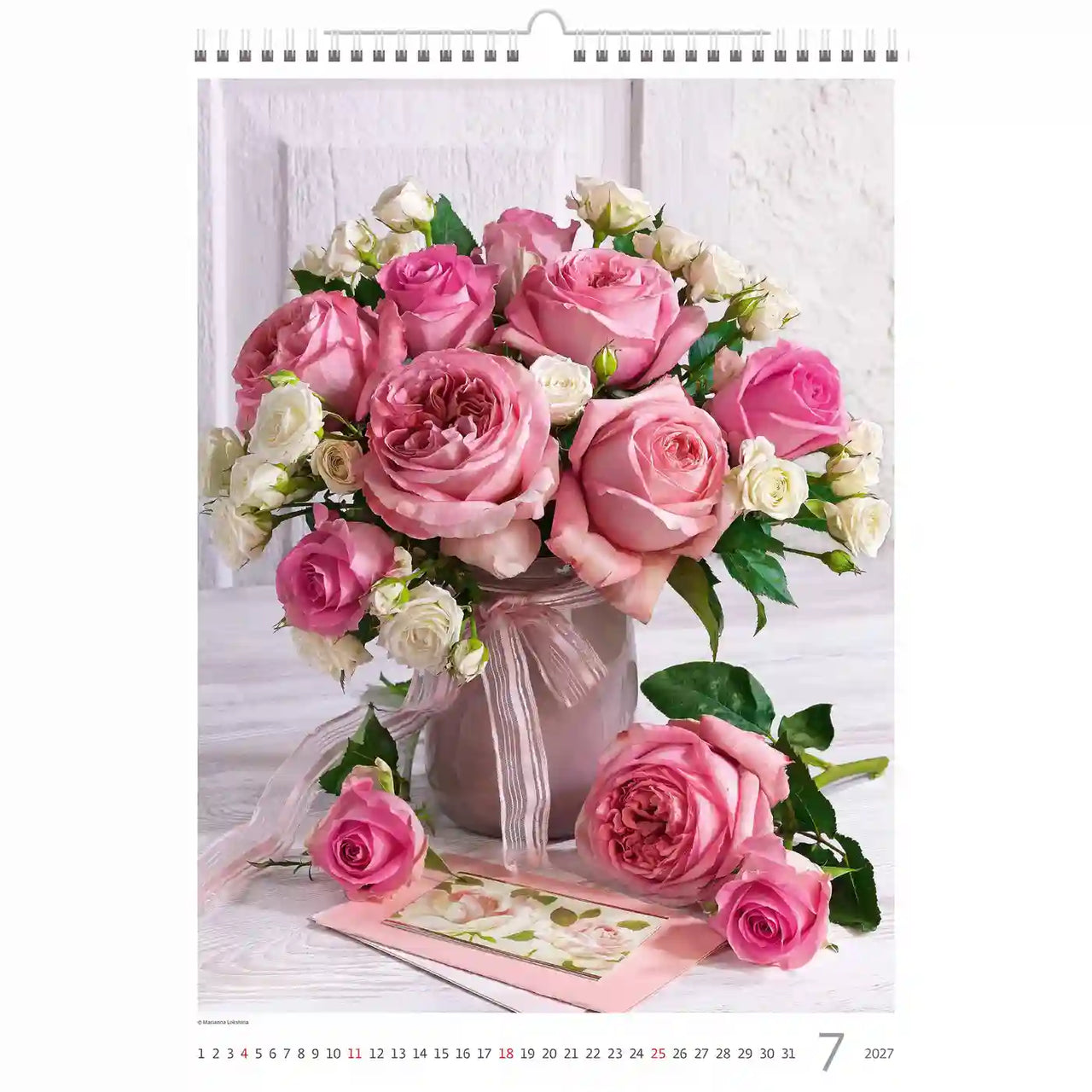 Bloemstuk met roze en witte rozen in een vaas op een houten ondergrond, met een kalender op de achtergrond.