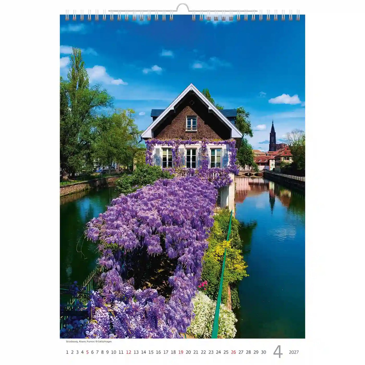 Kalenderpagina met een schilderachtig uitzicht op een huis aan een rivier met paarse bloemen.