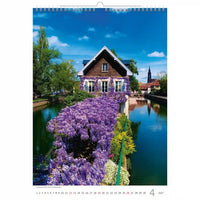 Kalenderpagina met een schilderachtig uitzicht op een huis aan een rivier met paarse bloemen.