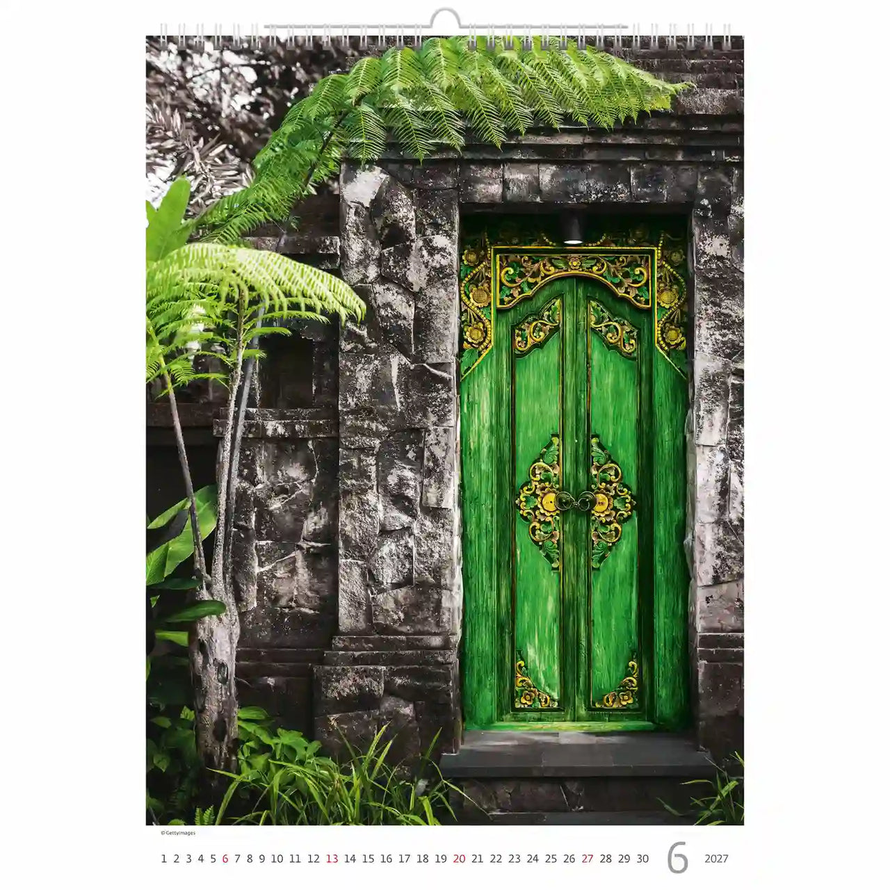 Groene deur met ingewikkelde ontwerpen op een stenen muur omgeven door groen, met een kalender indeling.