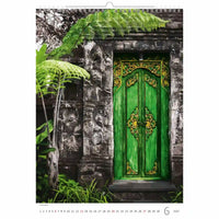 Groene deur met ingewikkelde ontwerpen op een stenen muur omgeven door groen, met een kalender indeling.