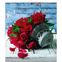 Bouquet de fleurs rouges avec un récipient en métal sur une surface rustique en bois contre un mur de briques bleues.
