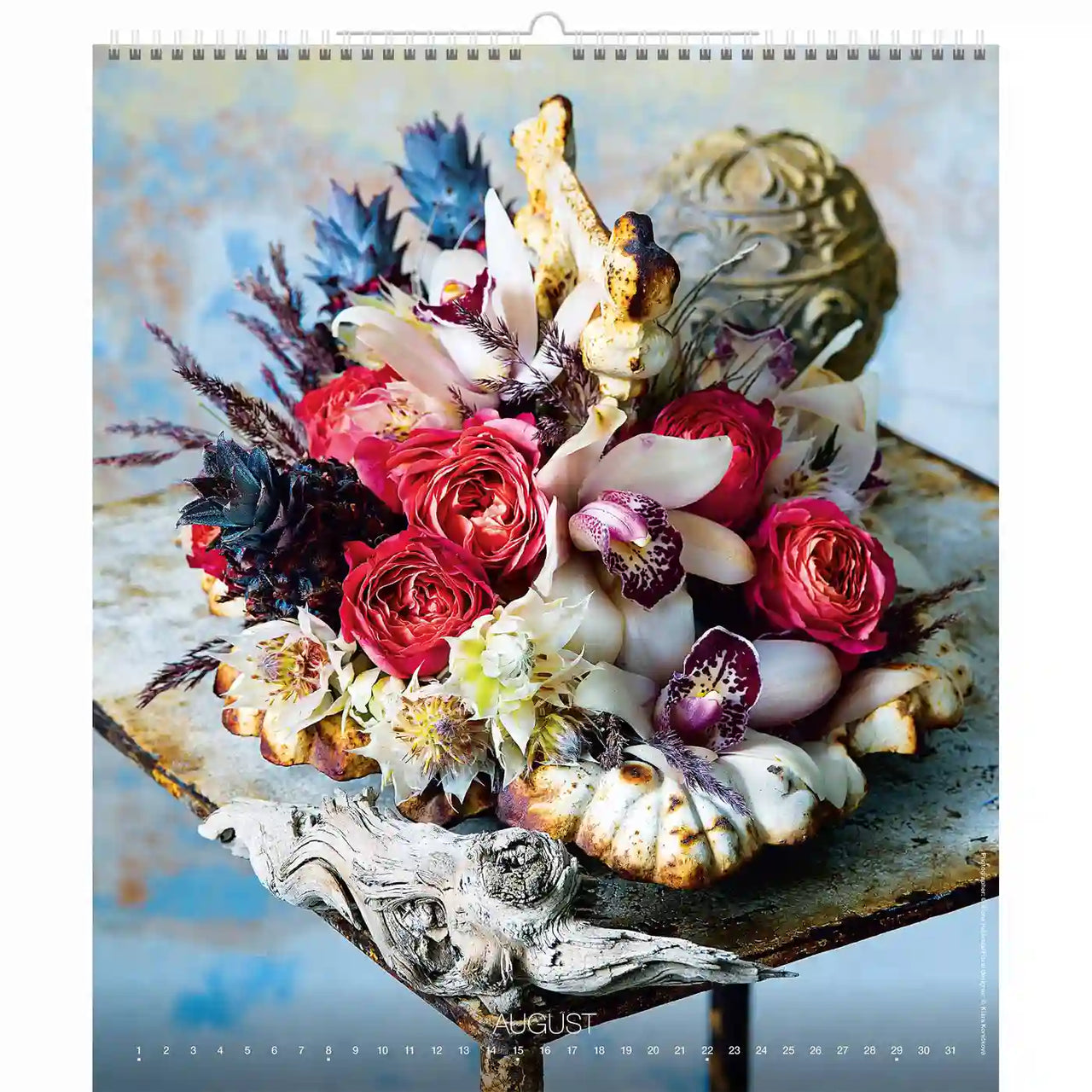 Arrangement floral avec des roses rouges et d'autres fleurs sur une surface décorative, représentant le mois d'août.